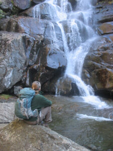 Christine sitting by water fall wearing backpack